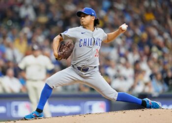 A Chicago Cubs pitcher in a grey uniform throws a baseball.