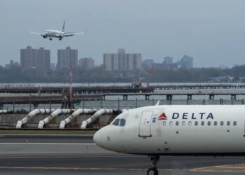 An American Airlines flight lands as a Delta Air Lines plane taxis at LaGuardia Airport in New York.