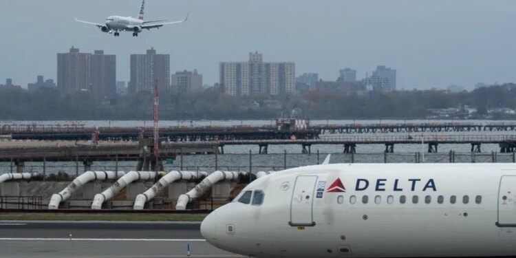 An American Airlines flight lands as a Delta Air Lines plane taxis at LaGuardia Airport in New York.