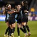 Rose Lavelle is mobbed by teammates after scoring a goal during a NWSL soccer match.