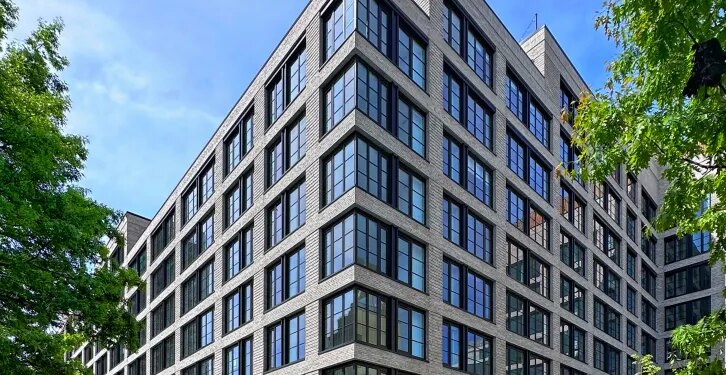 499 President Street in Gowanus, Brooklyn, a modern gray brick building with multiple large windows, with cars parked on the street in front and trees lining the street.