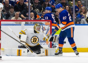 Boston Bruins goalie Jeremy Swayman making a save with New York Islanders player Anders Lee nearby.