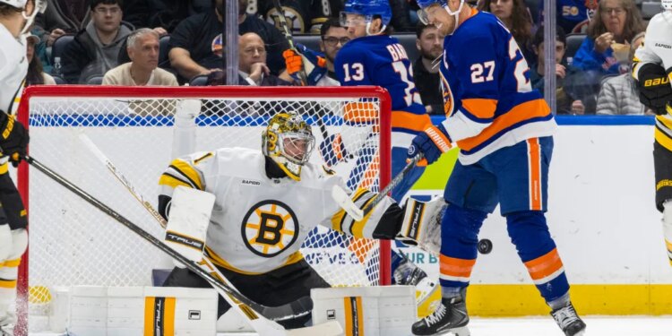 Boston Bruins goalie Jeremy Swayman making a save with New York Islanders player Anders Lee nearby.
