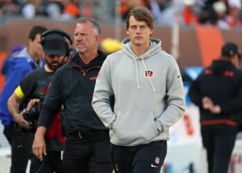 Joe Burrow, quarterback for the Cincinnati Bengals, wearing a grey hoodie and black sweatpants, walks on the sidelines during a game against the New York Jets.
