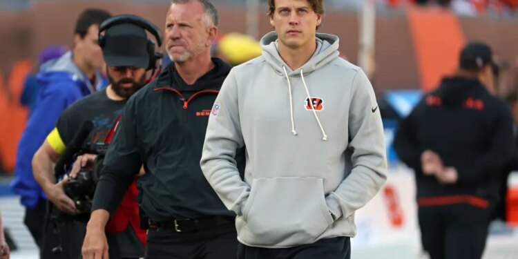 Joe Burrow, quarterback for the Cincinnati Bengals, wearing a grey hoodie and black sweatpants, walks on the sidelines during a game against the New York Jets.