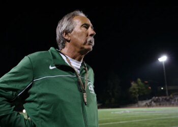 John Beam, in a green jacket, looking out at a football field at night.