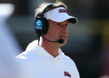 Lane Kiffin, head coach of the Mississippi Rebels, wears a white visor and a headset while looking on.