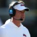 Lane Kiffin, head coach of the Mississippi Rebels, wears a white visor and a headset while looking on.