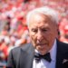 ESPN analyst Lee Corso wearing a black suit and bow tie, with an American flag lapel pin, leaving the field after his final pick.