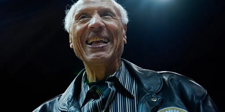 Lenny Wilkens smiling while wearing a black leather jacket over a striped shirt.