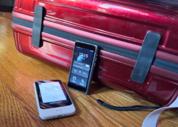 The Pocketalk (white) and Timekettle T1 propped against a red hardcase carryon luggage.