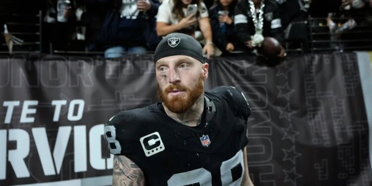 A Dallas Cowboys football player in a black jersey with number 98, a black skull cap, and a red beard looks ahead, as fans watch from behind a fence.