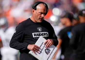 Tom McMahon in a black Raiders shirt, holding a white binder that reads "2024 Special Teams Sideline Notebook Tom McMahon."