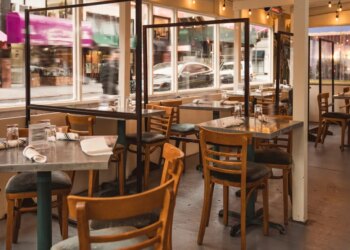 Outdoor dining area of a New York City restaurant set up on a sidewalk with empty tables and transparent partitions.
