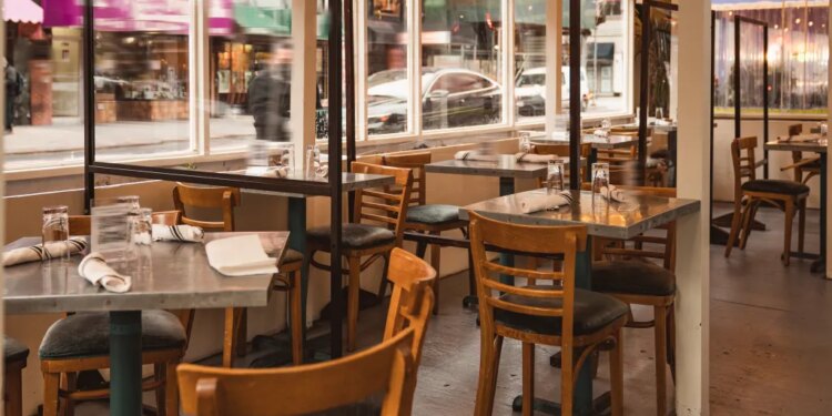 Outdoor dining area of a New York City restaurant set up on a sidewalk with empty tables and transparent partitions.