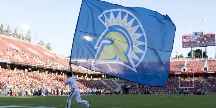 A San Jose State Spartans flag bearer runs with a large blue flag with a yellow and white Spartan logo across a football field.