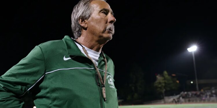 John Beam in a green and white track jacket, standing on a football field at night.