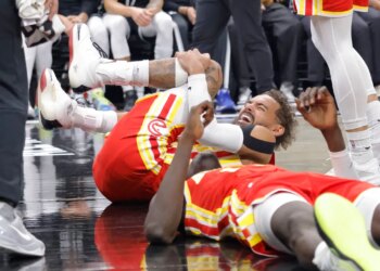 Trae Young of the Atlanta Hawks grimacing in pain while holding his knee on the court.