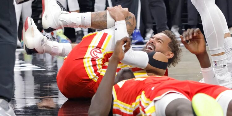 Trae Young of the Atlanta Hawks grimacing in pain while holding his knee on the court.