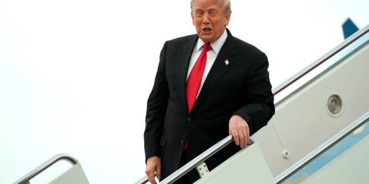 Donald Trump walking down the steps of Air Force One, speaking, wearing a black suit and red tie.