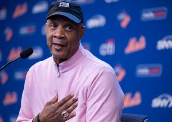 Darryl Strawberry speaking at a press conference, wearing a black cap, pink shirt, and championship ring.