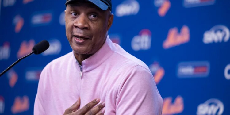 Darryl Strawberry speaking at a press conference, wearing a black cap, pink shirt, and championship ring.