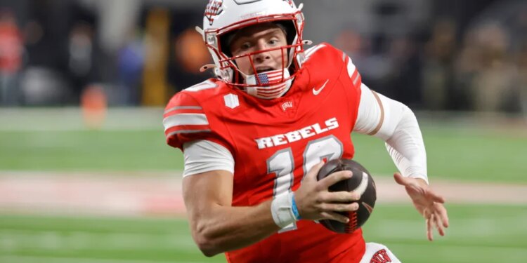 UNLV football player with number 10, wearing a red jersey, white helmet, and American flag chinstrap, running with the ball.