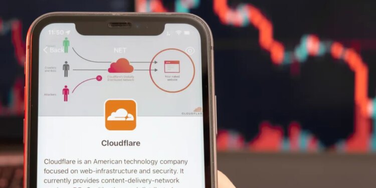 Hands holding a smartphone displaying Cloudflare's security process and company information, with a red stock market downtrend graph in the background.