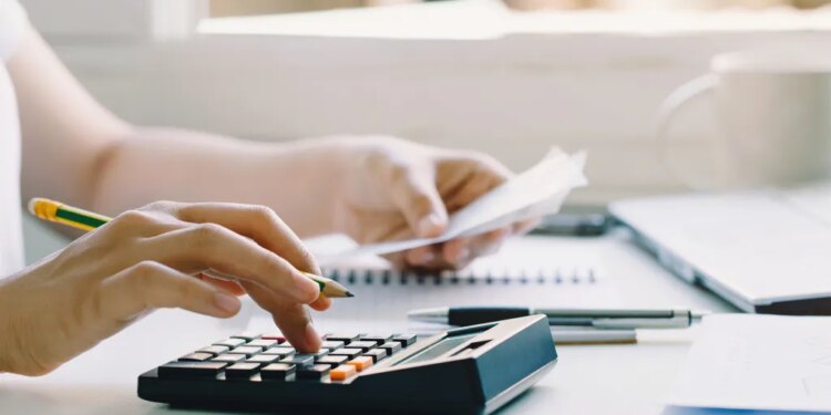A person uses a calculator and holds a bill, doing paperwork on a desk.