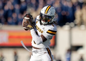 A Wyoming football player in a white uniform and helmet catching a football.