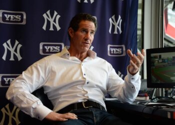 Paul O'Neill speaking with a monitor showing a baseball game and New York Yankees and YES Network logos in the background.