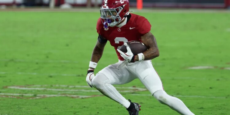 A football player in a red jersey and white pants running with the ball on a green field.