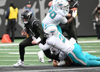 Jets quarterback Brady Cook (4) running with the ball as a Miami Dolphins player tackles him.