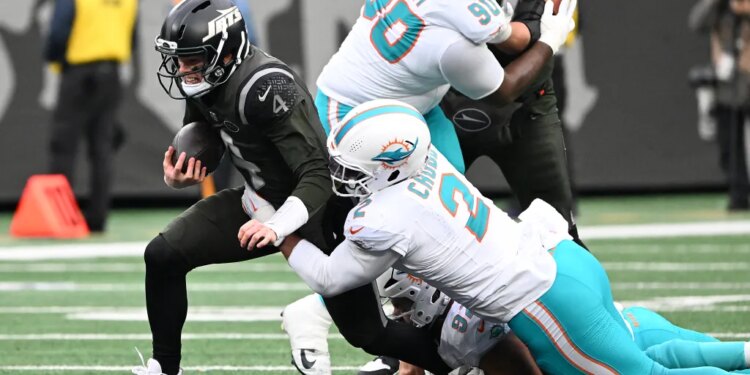 Jets quarterback Brady Cook (4) running with the ball as a Miami Dolphins player tackles him.