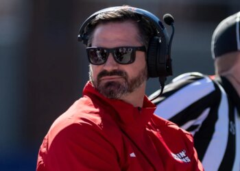 Louisiana head coach Michael Desormeaux wearing sunglasses and a headset, looking back at his bench.
