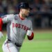 A Boston Red Sox player wearing a helmet and a grey uniform with "BOSTON" written in red on the front, running on a green baseball field.
