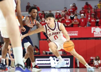 St. John's Red Storm player Dylan Darling dribbles the basketball while being guarded by a Bucknell Bison player.