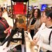 A Macy's employee helping two women with last-minute Christmas shopping at a perfume counter.