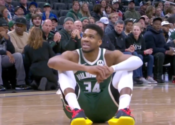 Basketball player Giannis Antetokounmpo sitting on the court during a game.