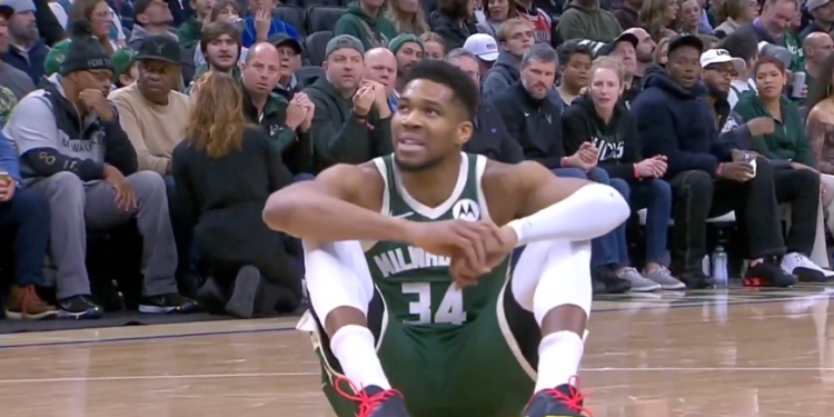 Basketball player Giannis Antetokounmpo sitting on the court during a game.