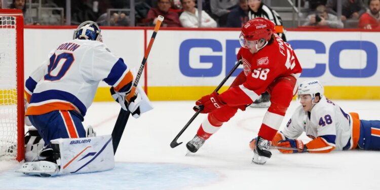 Detroit Red Wings center Emmitt Finnie (58) skates with the puck defended by New York Islanders defenseman Matthew Schaefer (48) in the second period at Little Caesars Arena.