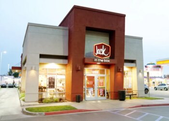 A Jack in the Box restaurant with a lit-up "Jack in the Box" sign on its red and beige facade.