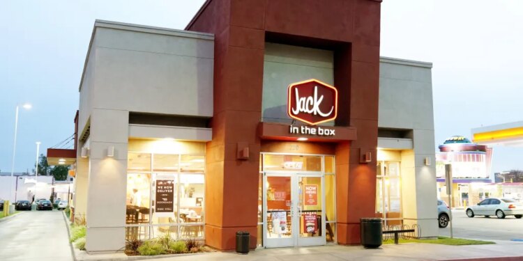 A Jack in the Box restaurant with a lit-up "Jack in the Box" sign on its red and beige facade.