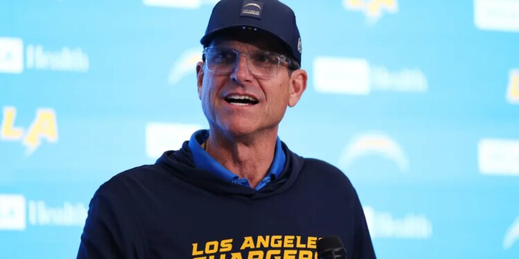 Jim Harbaugh of the Los Angeles Chargers wearing a cap and sweatshirt with team logos.