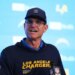 Jim Harbaugh of the Los Angeles Chargers wearing a cap and sweatshirt with team logos.