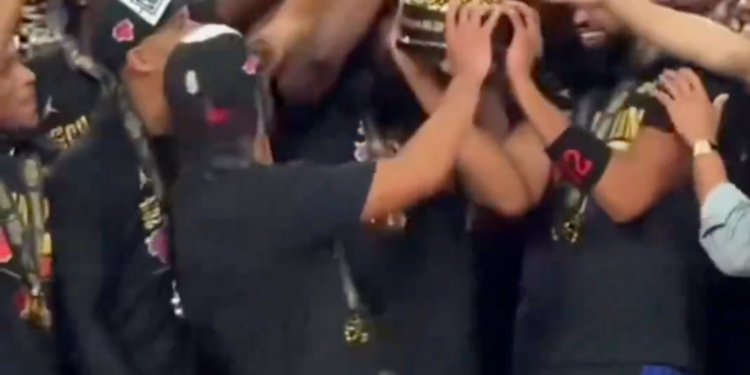 Josh Hart celebrating with his team while holding up a championship trophy.