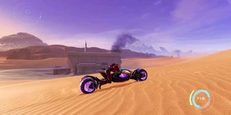 Screenshot from Metroid Prime 4 featuring Samus in the desert on a futuristic bike with a smoking ruin in the background.