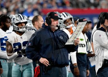 Dallas Cowboys head coach Mike McCarthy on the sideline holding a play chart.