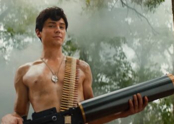 Miles Heizer as Cameron Cope, shirtless with an ammunition belt over his shoulder and a large weapon, in a misty forest.
