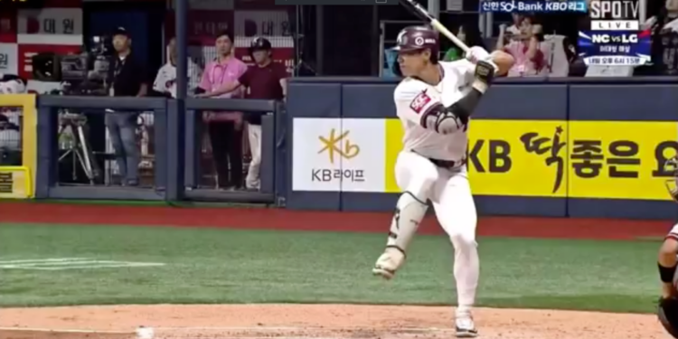 A baseball player in a white uniform with a maroon helmet and a bat in hand, standing at home plate, with "KB" and "KB LIFE" visible on the surrounding signage.